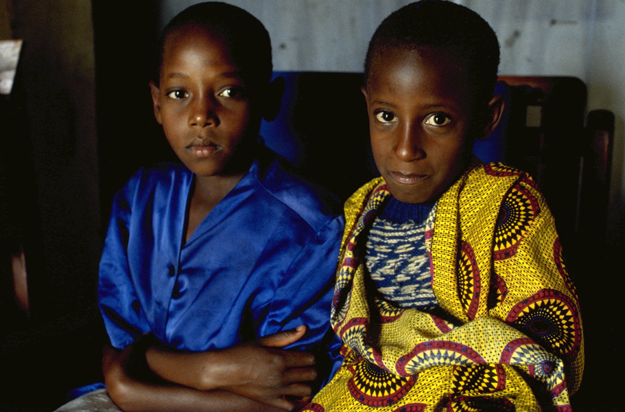 Two dark-skinned young brothers in blue and yellow clothes sit side by side